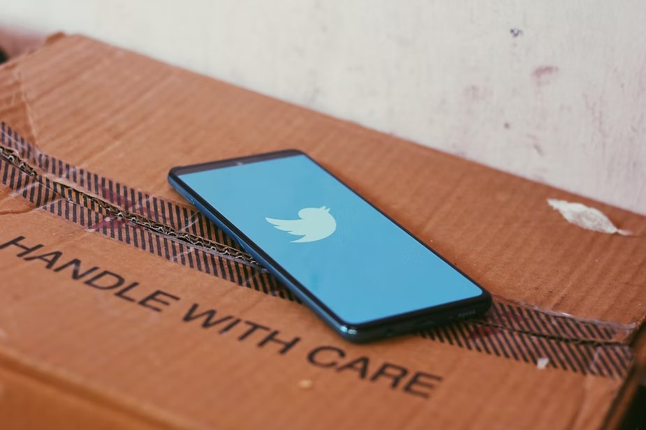Celular exibindo o logo do Twitter sobre uma caixa de papelão com 'Handle with care'