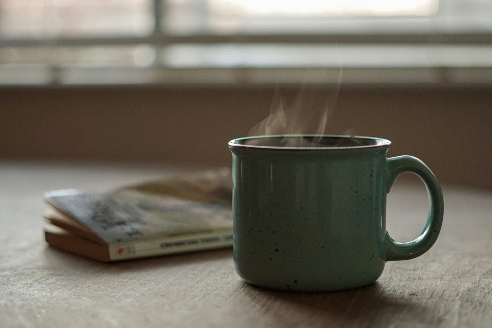 Caneca de chá fumegante ao lado de um livro, sobre uma mesa de madeira