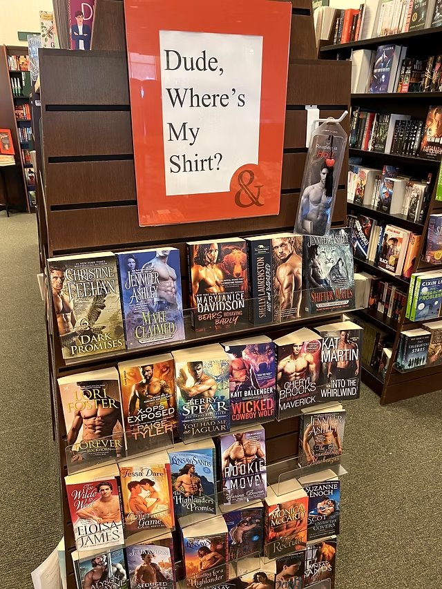 Display de livraria com o cartaz 'Dude, Where's My Shirt?' e capas de romance com homens sem camisa